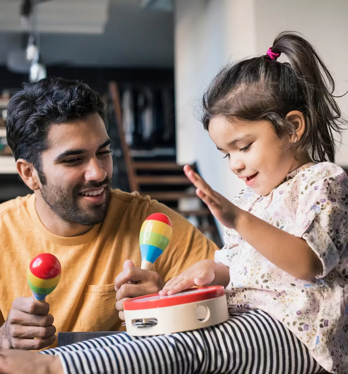 A parent and child playing music together with maracas and a tambourine